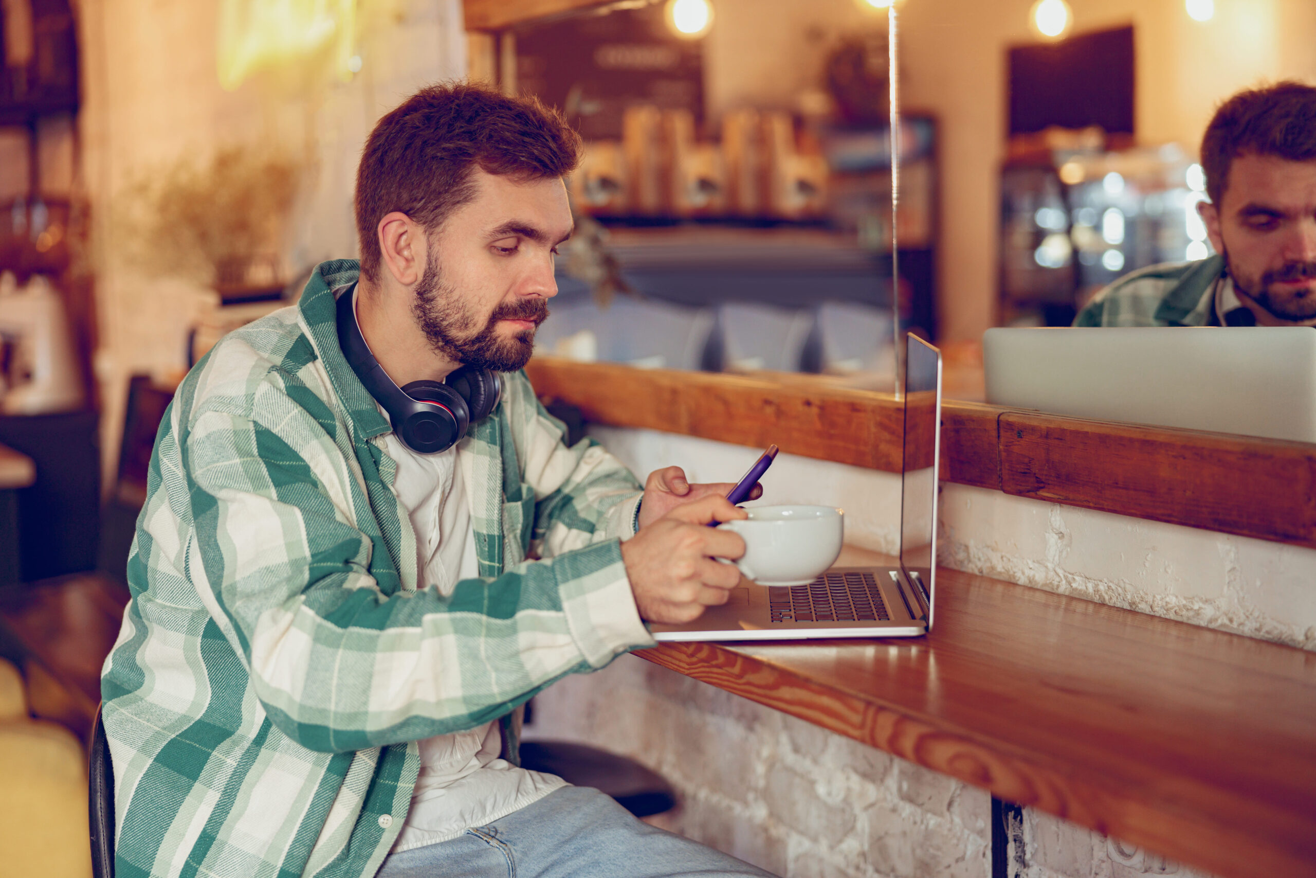 Hombre barbudo con ordenador portátil y teléfono móvil en café