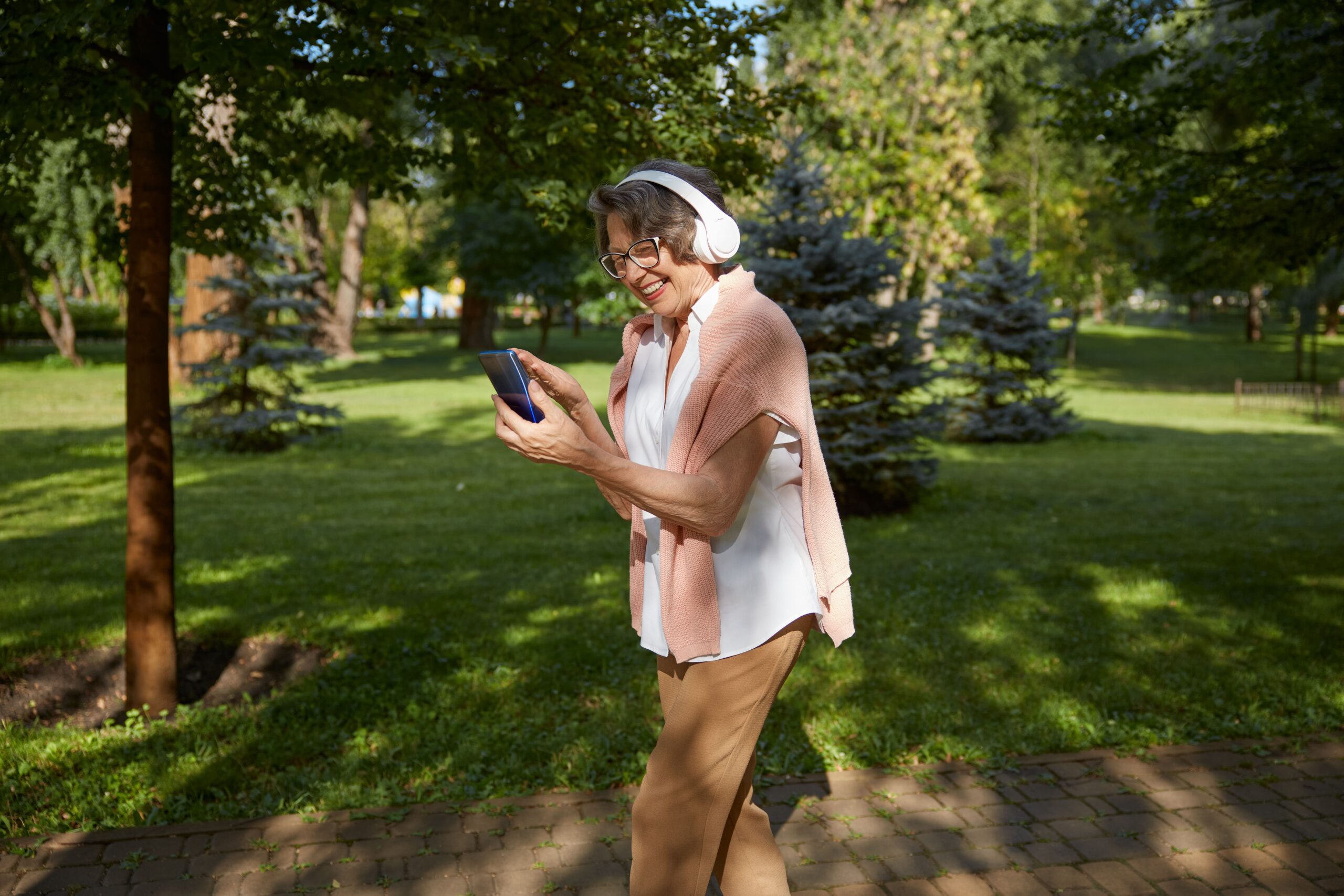 Mujer de edad avanzada usando su celular en un parque mientras camina